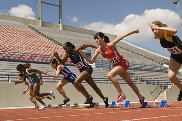 Group of diverse runners taking off from starting blocks in race