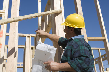 Happy mature architect with blueprint inspecting at construction site