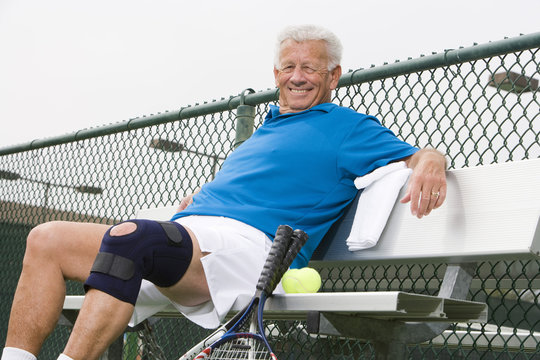 Portrait of a happy senior man relaxing on bench after playing tennis