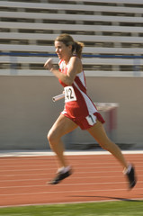 Full length of female athlete running with baton in race track