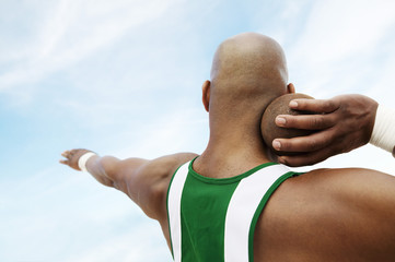 Closeup rear view of a shot putter preparing to toss shot put against the sky