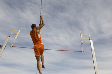 Low angle view of a male athlete performing a pole vault against the sky