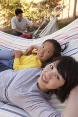 Portrait of mother and daughter relaxing on hammock with father in the background