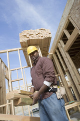 Portrait of foreman carrying wooden beam at construction site