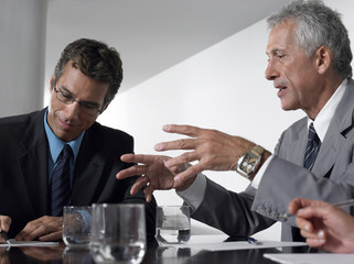 Businessman conversing while male colleague taking notes in conference room