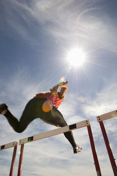 Low angle view of a male athlete jumping hurdle against the sky