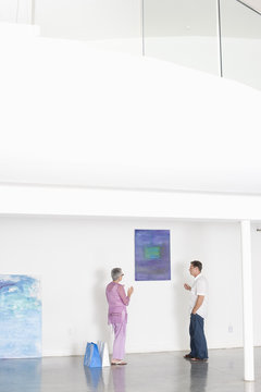 Full length of mature couple discussing over painting in art gallery