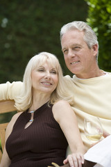 Middle aged couple relaxing on bench with wineglass outdoors