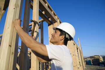 Side view of male construction worker hammering nail on wooden wall