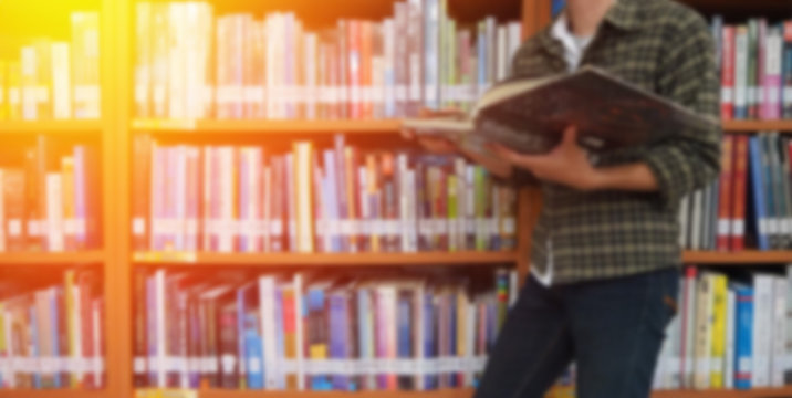 Reading book in library and abstract blur bookshelf in library room background, education concept