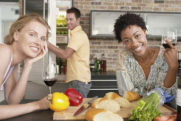 Smiling multiethnic women holding wine glasses at kitchen counter with man in background