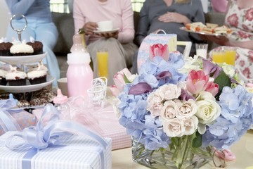 Bouquet and gifts on table with women in background at a baby shower