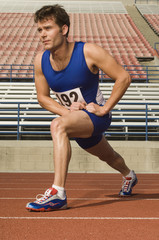 Full length of confident male athlete stretching in racing field