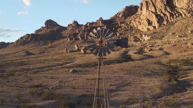 AERIAL: Flying over vintage windmill in sunny rocky mountain desert