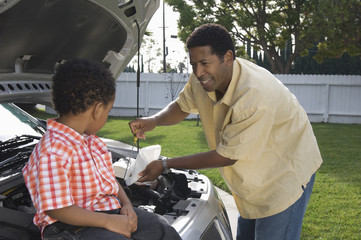 Little boy looking at father checking engine oil of a car