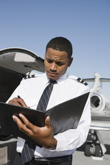 An airplane pilot taking notes on notepad with airplane in the background at airfield © MDBPIXS