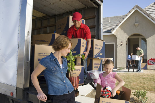 Family And Worker Unloading Truck Of Cardboard Boxes