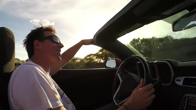 SLOW MOTION: Excited smiling man enjoying the summer day driving in convertible