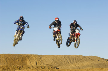 Three motocross male racers racing against clear blue sky