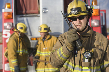 Portrait of a middle aged firefighter talking on radio with colleagues standing in the background