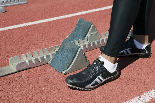 Low section of male athlete at starting block on racetrack