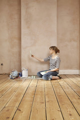 Side view of woman with painting tools choosing color from swatches in unrenovated room