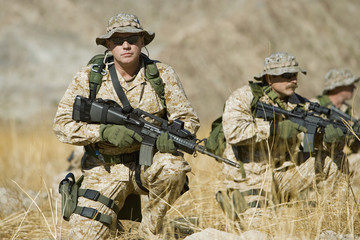 Portrait of confident soldier with rifle while team patrolling in background during war