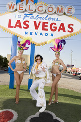 Portrait of Elvis Presley impersonator standing with casino dancers against sign board