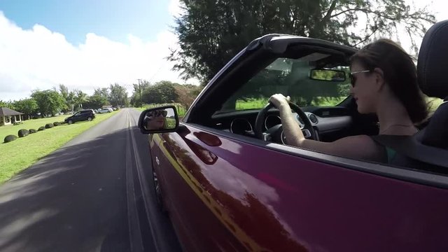 SLOW MOTION: Young woman in red convertible driving through Hawaii village