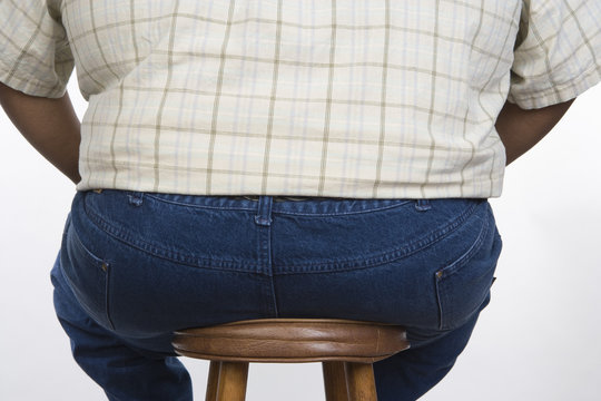 Rear view of an obese man sitting on a stool isolated over white background