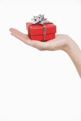 Closeup of a hand holding up small wrapped gift against white background