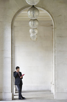 Full Length Of Young Businessman Using Cell Phone While Leaning In Archway