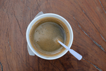A coffee in a paper cup on wooden table.