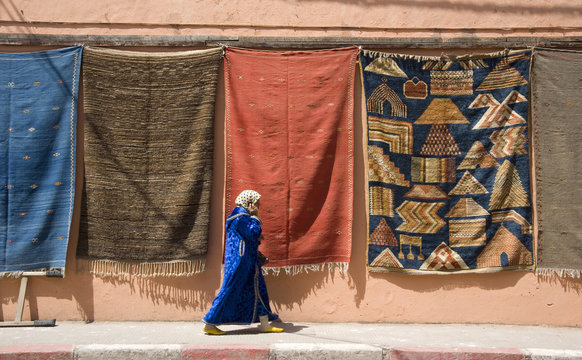 A woman in Islamic dress walking by a wall hung with carpets in the Medina in Marrakech, Morocco