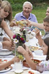 Cheerful senior man with family dining together in garden