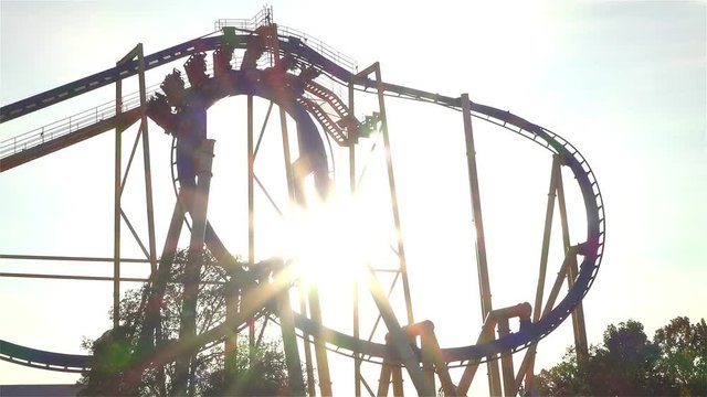 SLOW MOTION: People riding extreme roller coaster over the sun
