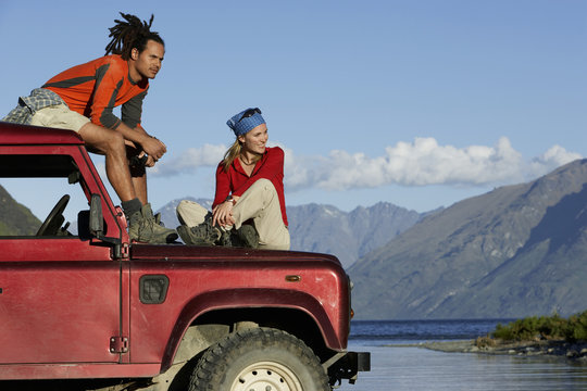 Man and woman sitting on top of jeep near mountain lake