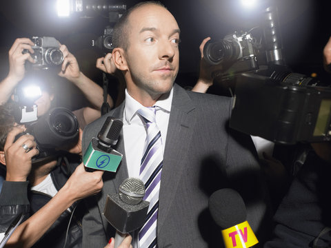 Displeased man in suit surrounded by paparazzi