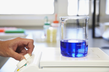 Human hand analyzing scientific glass container filled with blue liquid on scale