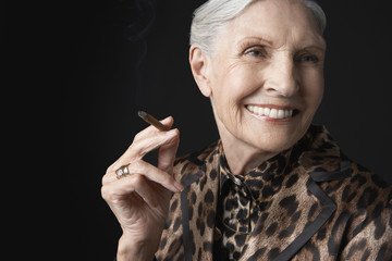 Closeup of an elegant senior woman smoking cigarillo against black background