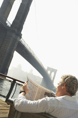 Man reading newspaper with Brooklyn bridge against the sky