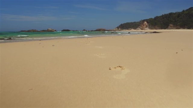 AERIAL: Footsteps in sandy beach leading into crystal clear blue ocean lagoon