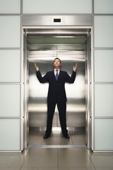 Full length of middle aged businessman with arms raised looking up while standing in elevator