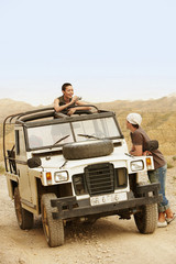Young woman taking photograph of man standing by four-wheel-drive car