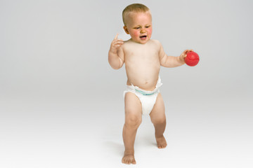 Full length of baby boy with red ball walking isolated on gray background