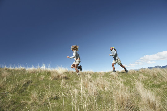 Full length side view of a man and woman running through field against blue sky