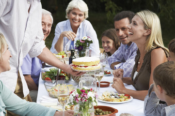 Three generation family celebrating birthday of woman at dining table outdoors