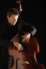 Young man playing double bass against black background