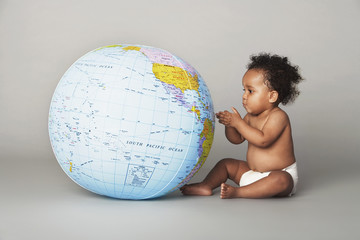Full length of baby girl looking at inflatable globe isolated on gray background
