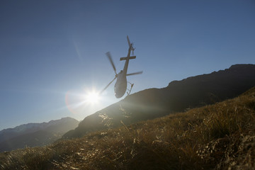 Low angle view of a helicopter flying over hills in front of the sun